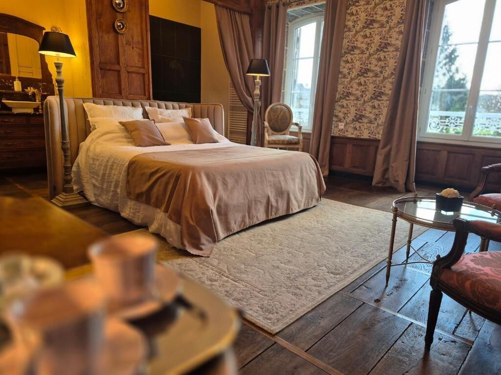 A bedroom with a large bed, a wooden dresser, a chair, and a window with curtains.
