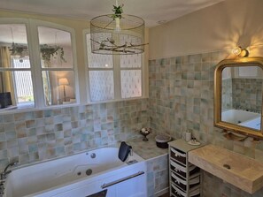 A bathroom with a bathtub, a vanity with a mirror, and a wall-mounted light fixture. - La Bâtisse de Bromont (Bromont-Lamothe)
