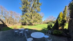 A patio with metal tables and chairs, surrounded by trees and a grassy area.