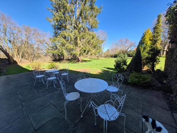 A patio with metal tables and chairs, surrounded by trees and a grassy area. - La Bâtisse de Bromont (Bromont-Lamothe)