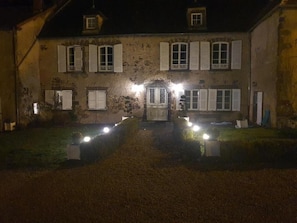 Un bâtiment historique doté d’une entrée centrale, de nombreuses fenêtres avec volets et d’une allée gravillonnée.