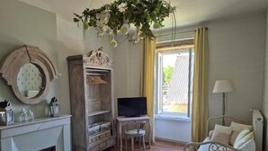 A bedroom with a bed, a television, a wooden wardrobe, a small table, a chair, and a window with curtains.