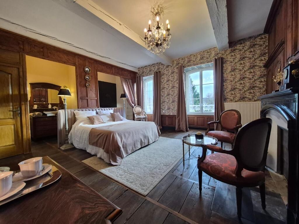 A bedroom with a bed, a chair, a table, and a chandelier.