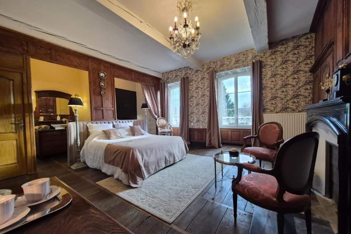 A bedroom with a bed, a chair, a table, and a chandelier.