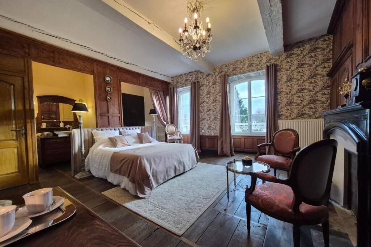 A bedroom with a bed, a chair, a table, and a chandelier.