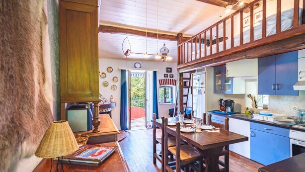 Eine rustikale Küche mit Holzsäulen, einem Esstisch und einer Treppe, die auf einen Balkon führt.