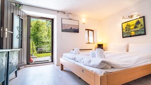 Ein Schlafzimmer mit einem Holzbett, einem kleinen Schreibtisch, einer Tür, die auf einen Balkon führt, und einem Bild an der Wand.