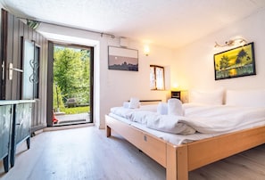 Ein Schlafzimmer mit einem Holzbett, einem kleinen Schreibtisch, einer Tür, die auf einen Balkon führt, und einem Bild an der Wand.