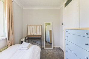 A bedroom with a bed, a dresser, a radiator, a mirror, and a 'HOLA!' sign. - Modern 2BDR Flat w Parking Near Heathrow and Tube (London)