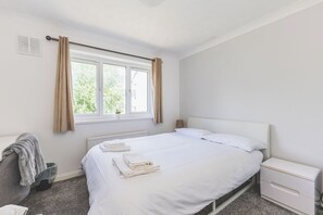 Une chambre d’hôtel propre et blanche, avec un lit, des tables de chevet, un radiateur et une fenêtre avec des rideaux.