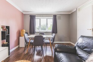 A cozy living room with a dining area, a black leather sofa, and a bookshelf. - Modern 2BDR Flat w Parking Near Heathrow and Tube (London)