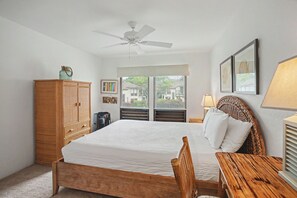Ein Schlafzimmer mit Bett, Holz-Kopfschild, einem Holztisch, Deckenventilator und einem Fenster mit Jalousien.