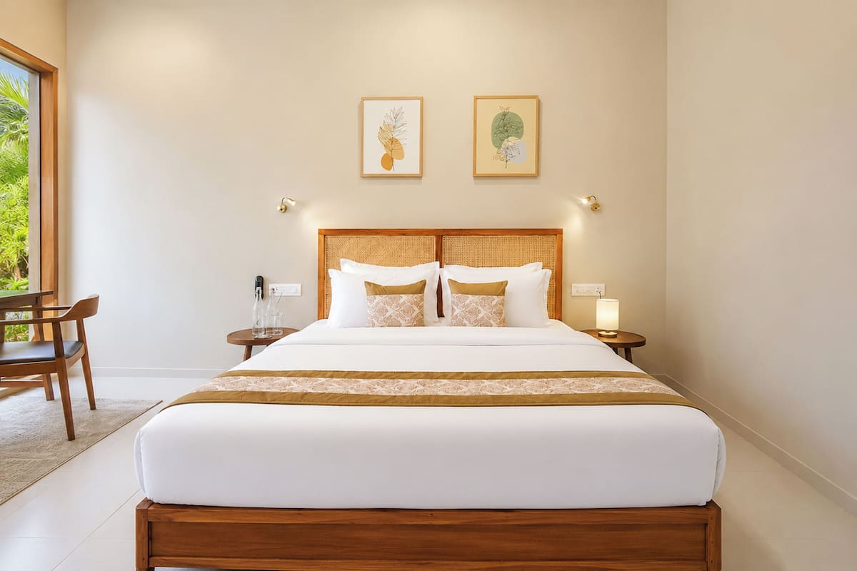 A hotel room with a large bed, two bedside tables, a chair, and two framed artworks on the wall.