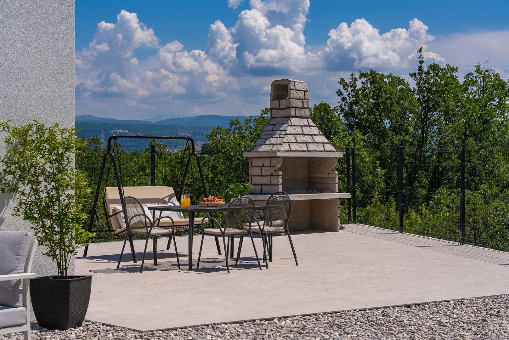 A patio with a stone barbecue, outdoor seating, and a view of the mountains.