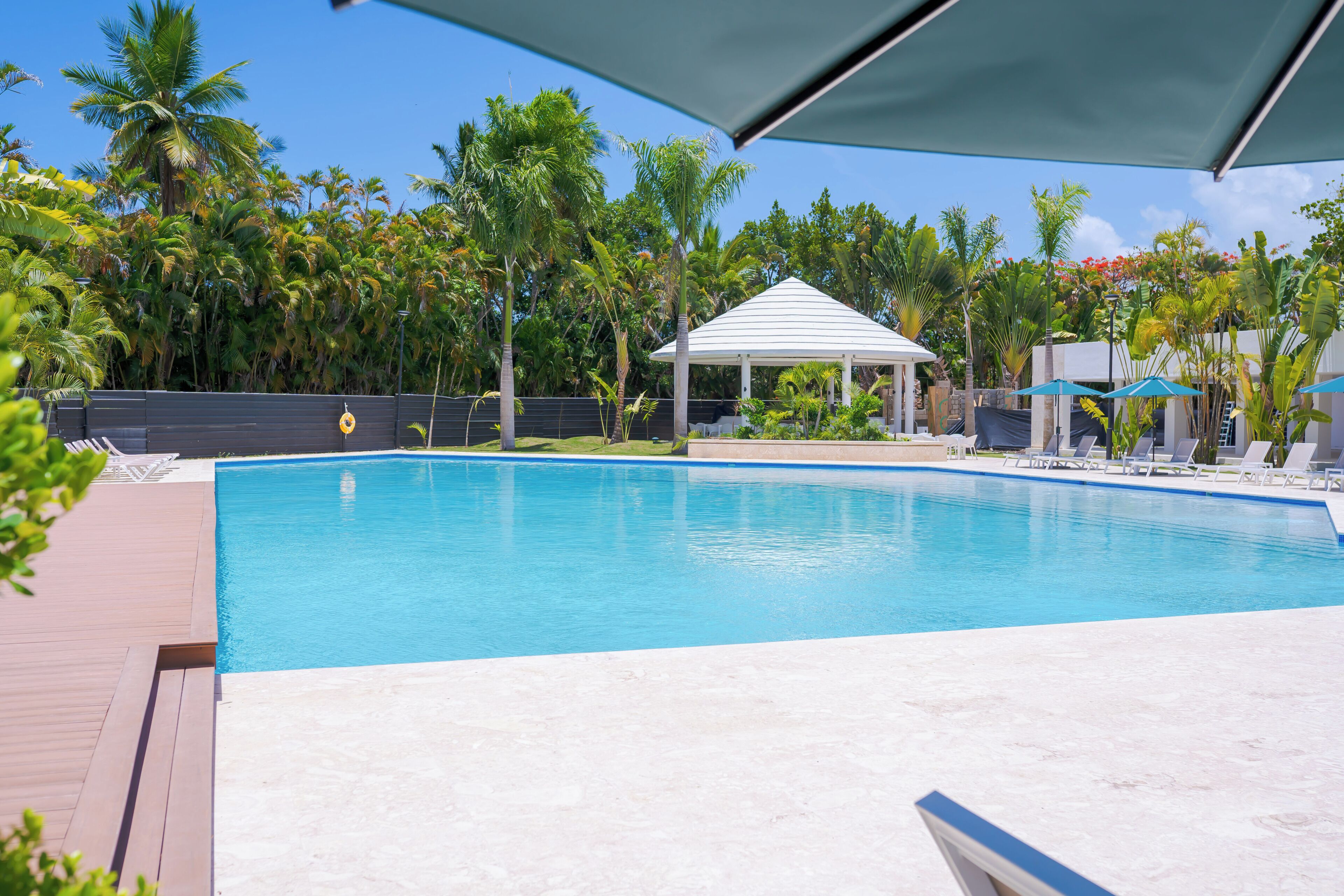 Una piscina con cubierta de madera, rodeada de palmeras y un pabellón.