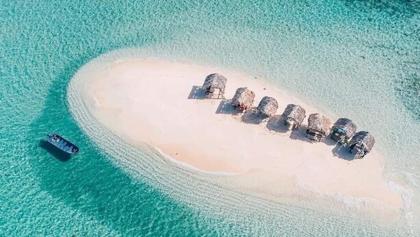 Vista aérea de una pequeña isla con una playa de arena y una hilera de chozas de techo de paja.