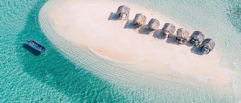 Vue aérienne d’une petite île avec une plage de sable et une rangée de huttes aux toits de chaume.