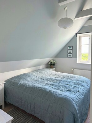 Et soveværelse med en stor seng, et vindue, en radiator og en lampe i loftet.