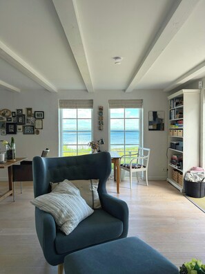 A room with a large window, a chair, a table, and a bookshelf. - Summer house in fisherman's style by Helnæs Bay (Ebberup)