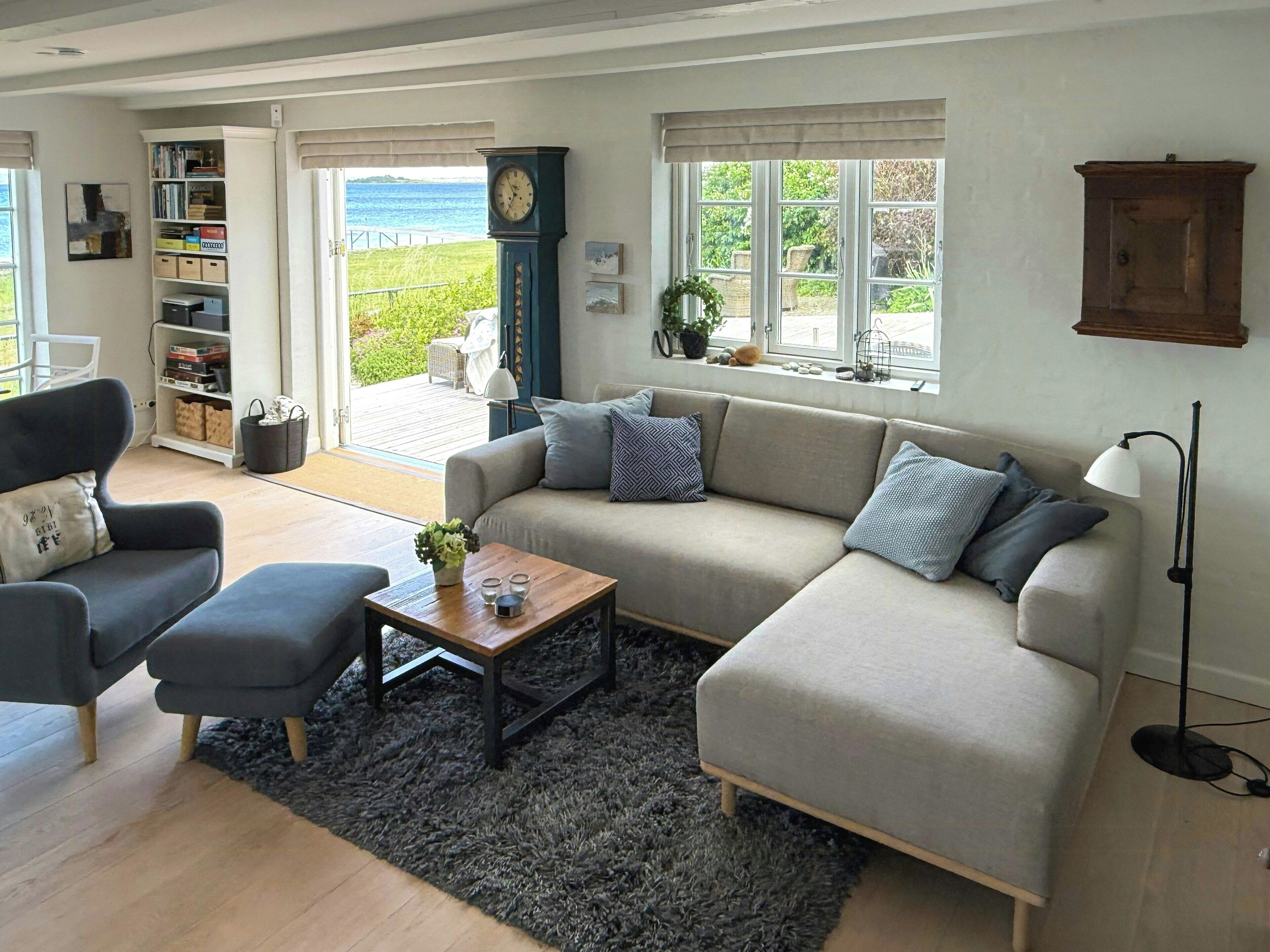 Una sala de estar con sofá, sillones, una mesita de centro, estantería, un reloj y vistas al exterior.