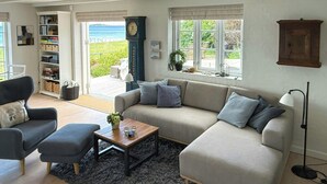A living room with a sofa, armchairs, a coffee table, a bookshelf, a clock, and a view of the outdoors.