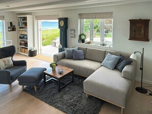 En stue med sofa, lænestole, et sofabord, en reol, et ur og udsigt til det fri.