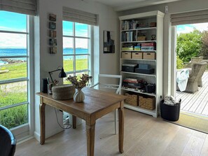 A room with a view of the sea, a wooden table with a vase, a bookshelf, and wicker furniture. - Summer house in fisherman's style by Helnæs Bay (Ebberup)