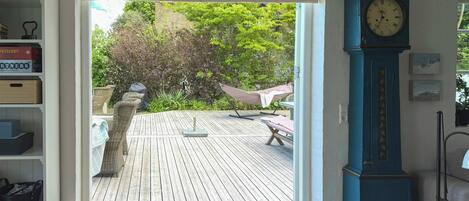 Ein offenes Durchgang zu einer Holzterrasse mit Gartenmöbeln, einer Uhr und einem Bücherregal mit Büchern.