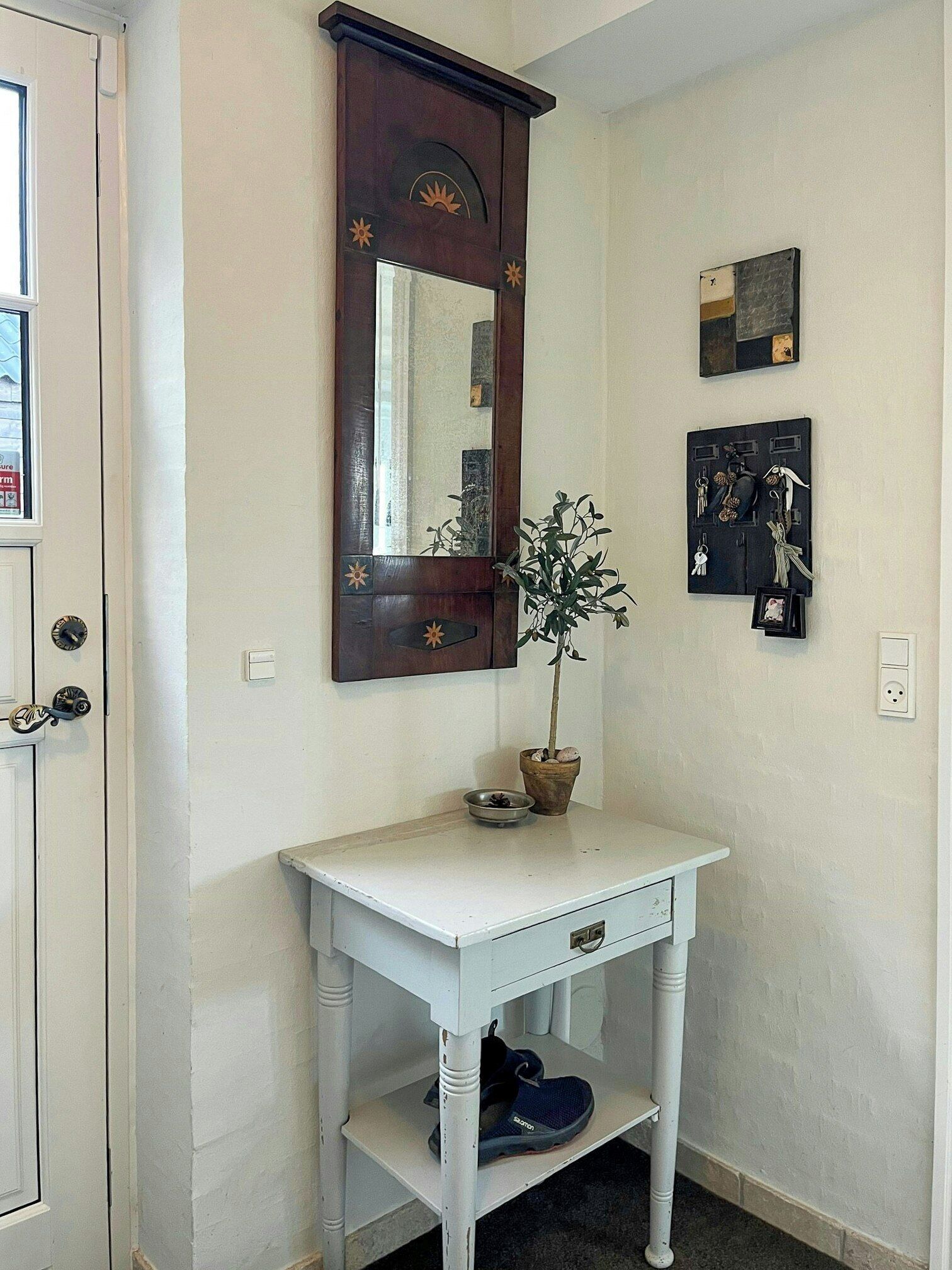 A white console table with a mirror, a potted plant, and a shoe rack.