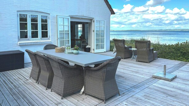 A deck with wicker furniture, a table, and a view of the ocean.