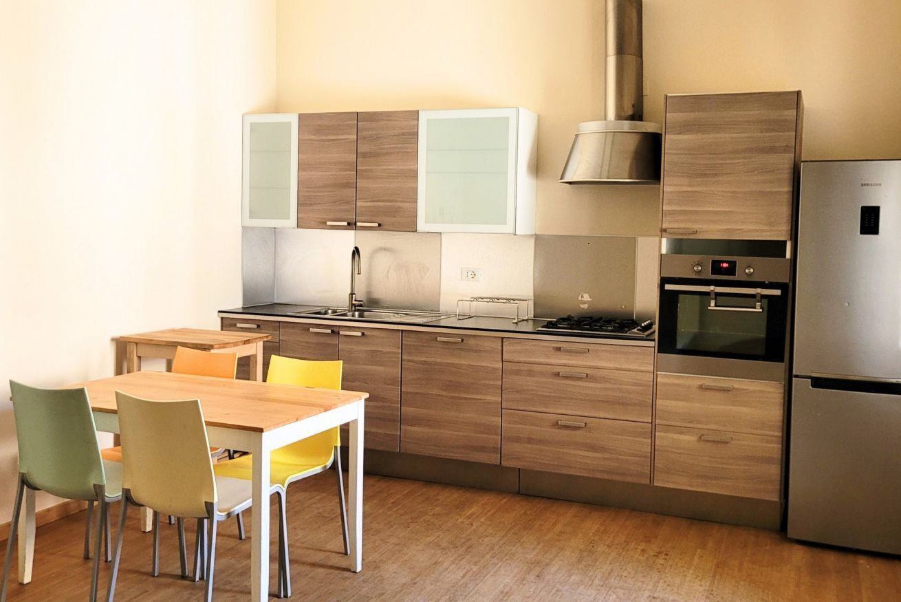 A modern kitchen with wooden cabinets, a stainless steel refrigerator, and a dining area with a wooden table and chairs.