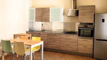 A modern kitchen with wooden cabinets, a stainless steel refrigerator, and a dining area with a wooden table and chairs.