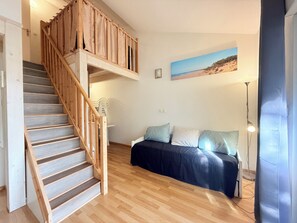 Ein Zimmer mit einer Holztreppe, einer Couch mit Kissen, einem Strandbild und einer Stehlampe.