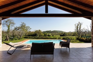 Eine Terrass mit Blick auf einen Pool, umgeben von Grünflächen und Hügeln.