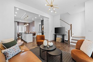 Ein modernes Wohnzimmer mit Sofa, Couchtisch und Fernseher, verbunden mit einer Küche und einem Essbereich.