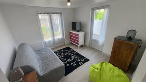 Une pièce avec un canapé, un téléviseur posé sur un meuble, une armoire en bois et un sac vert.