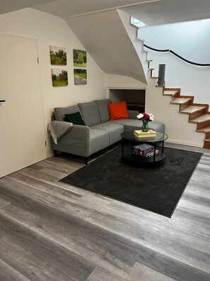 Una sala moderna con un sofá gris, una mesa de centro negra y una escalera.