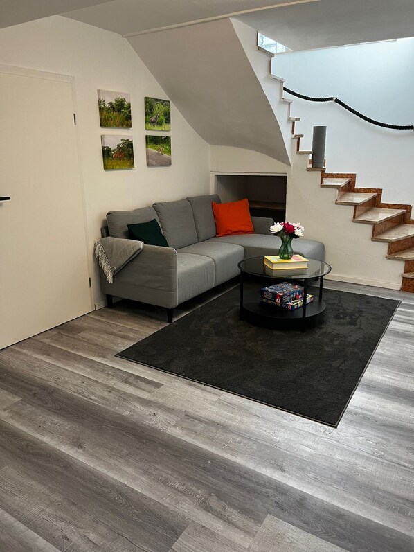 Ein modernes Wohnzimmer mit einem grauen Sofa, einem schwarzen Couchtisch und einer Treppe.