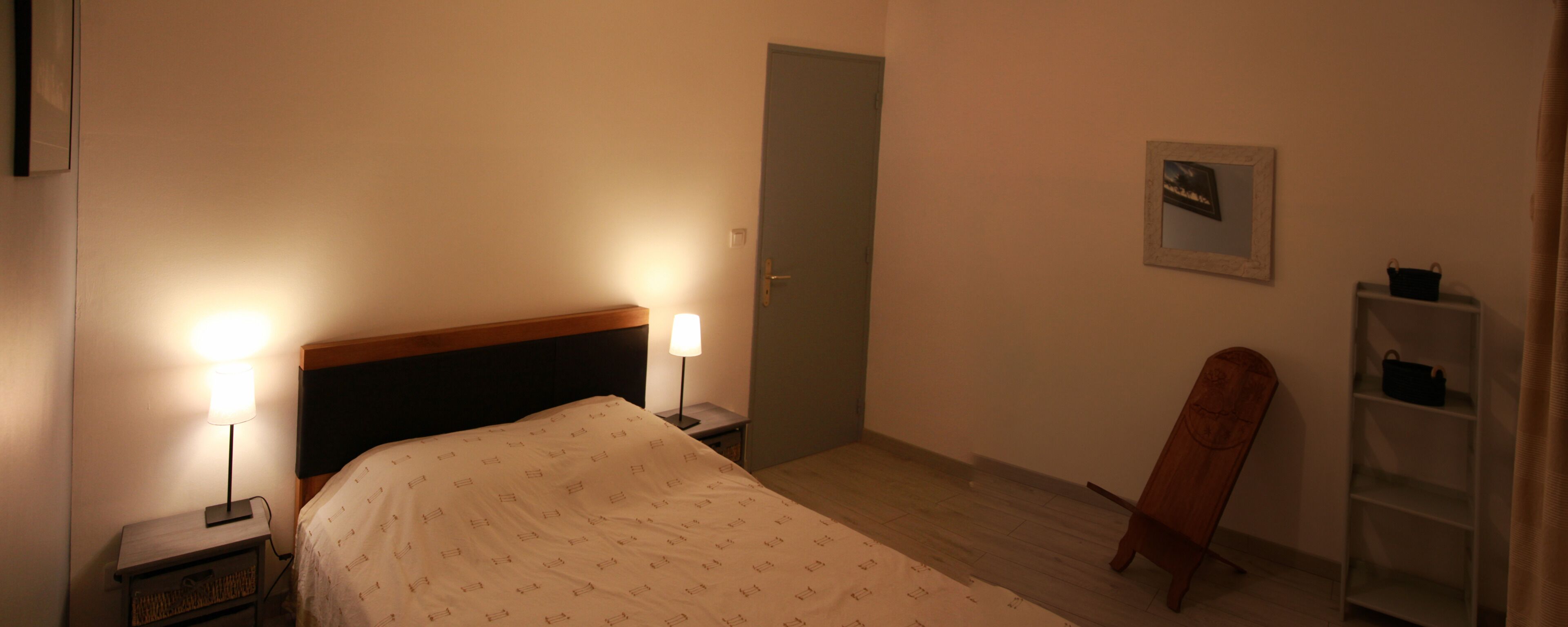 A bedroom with a bed, bedside lamps, a door, a wooden cabinet, and a framed picture on the wall.