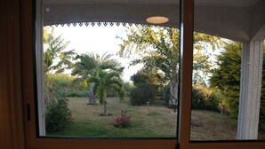 A window with a view of a garden with palm trees and shrubs. - Very large villa in Les Avirons: 6 bedrooms, sleeps 13, heated pool, and tropical garden (Les Avirons)