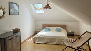 Ein Schlafzimmer mit schrägen Wänden, einem Bett mit blauen Kissen, einem Hängestuhl, einem Nachttisch mit Lampe und einem Bilderrahmen an der Wand.