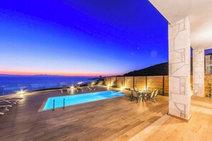 Zona de piscina en la azotea con vista al océano al atardecer.