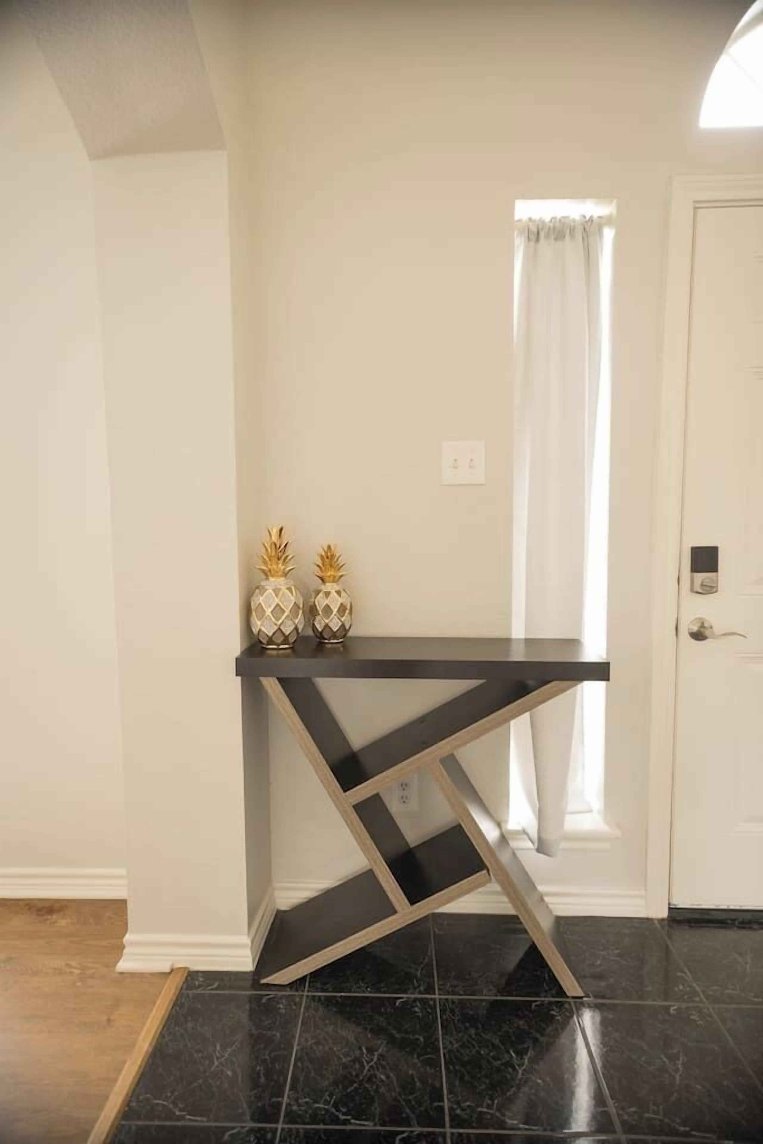 Une pièce avec une console noire, deux vases décoratifs, une porte blanche et une fenêtre avec des rideaux.