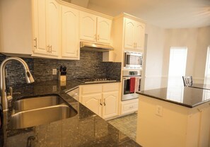 A kitchen with white cabinets, a granite countertop, a stainless steel sink, a built-in stove, and a microwave. - Spacious 4 Bedroom home with private backyard (Irving)