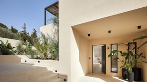 Een modern exterieur met een beige gevel, een trap in beige tinten die naar een deur leidt, en potplanten bij de ingang.
