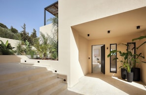A modern exterior with a beige facade, a set of beige stairs leading to a door, and potted plants near the entrance. - The Nook Luxury Villa (Agia Pelagia)
