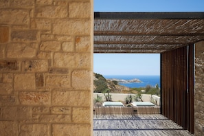 A stone wall with a wooden pergola and a view of the sea. - The Nook Luxury Villa (Agia Pelagia)