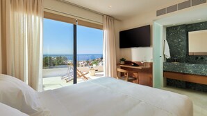 Een hotelkamer met een groot bed, een bureau, een flatscreen-tv, een badkamer met een marmeren aanrecht en een balkon met uitzicht op zee.
