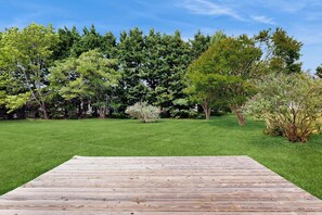 A wooden deck with a grassy lawn and trees in the background. - Rehoboth Beach - 1 Melody Ct (Rehoboth Beach)
