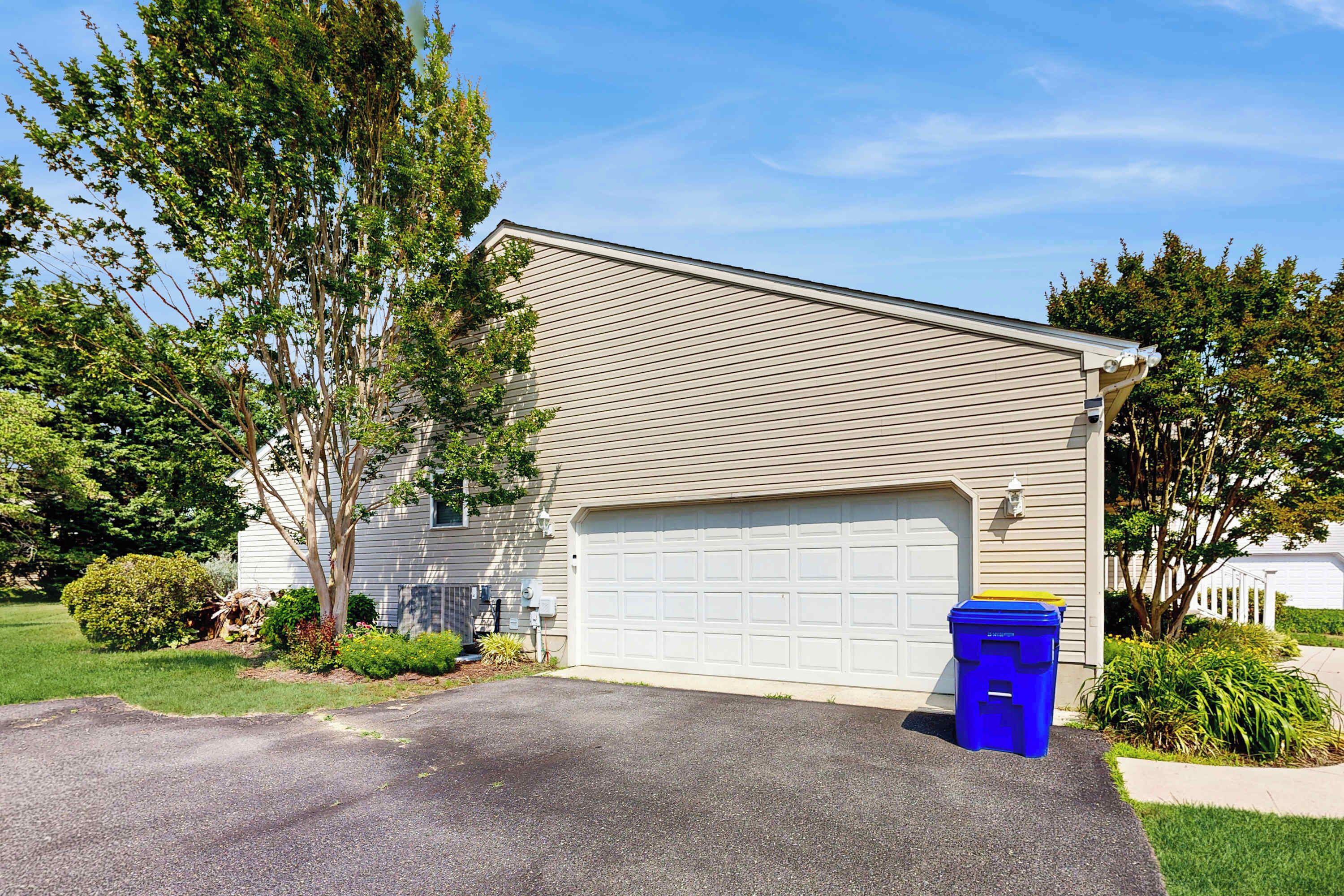A residential house with a garage, a driveway, and a blue trash bin.
